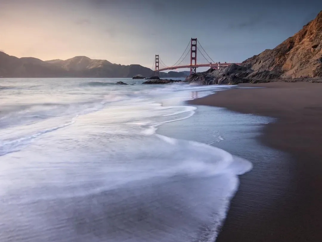 Surf on the sand below the Golden Gate Bridge at dusk